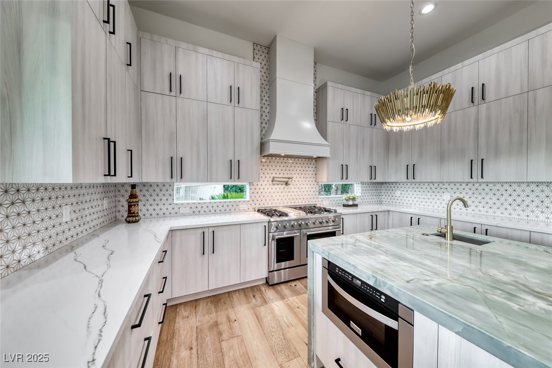 2309 Prometheus Court Henderson, NV 89074 - Photo 21 of 70 Kitchen featuring light stone countertops, custom exhaust hood, appliances with stainless steel finishes, light wood-style floors, and recessed lighting