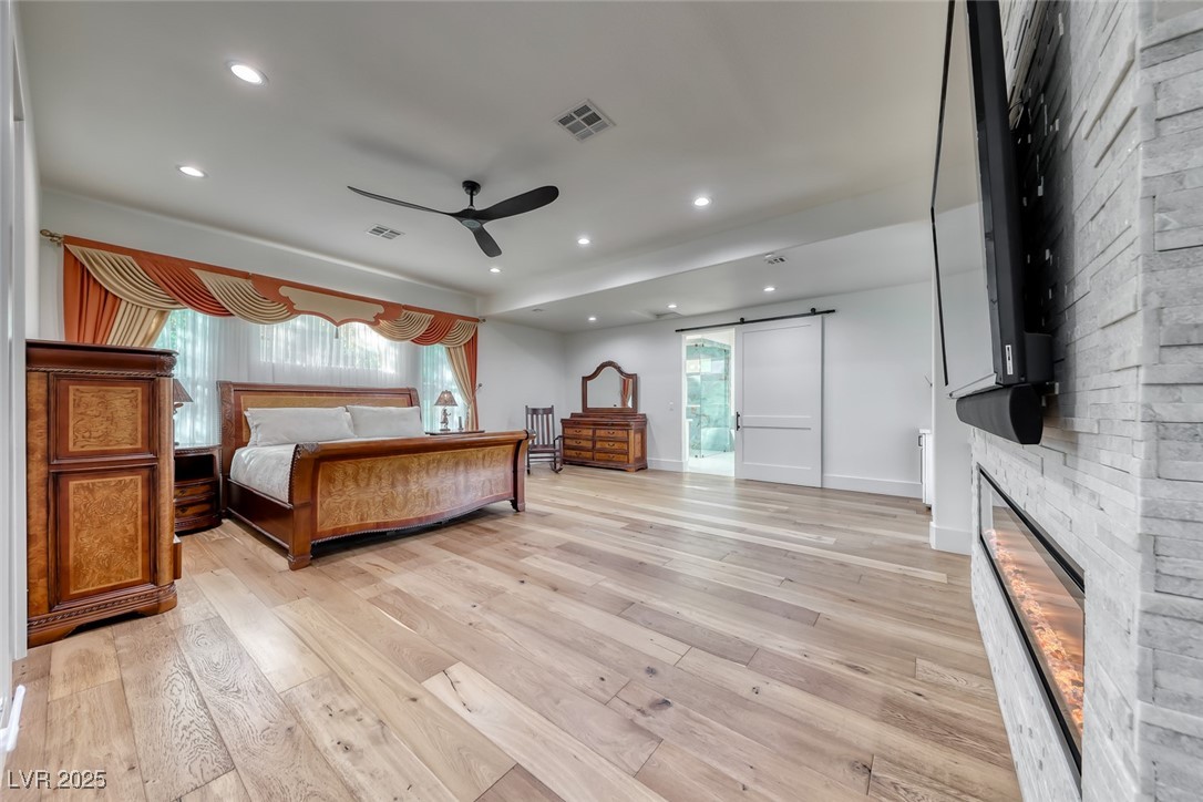 2309 Prometheus Court Henderson, NV 89074 - Photo 30 of 70 Bedroom featuring a barn door, light wood finished floors, recessed lighting, a ceiling fan, and a stone fireplace