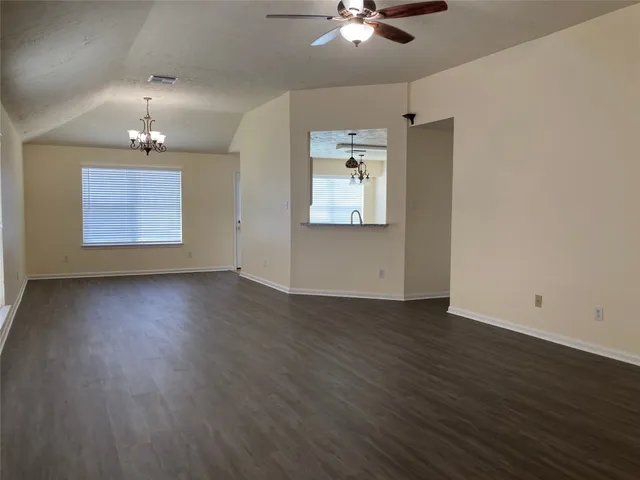 an empty room with wooden floor chandelier fan and windows