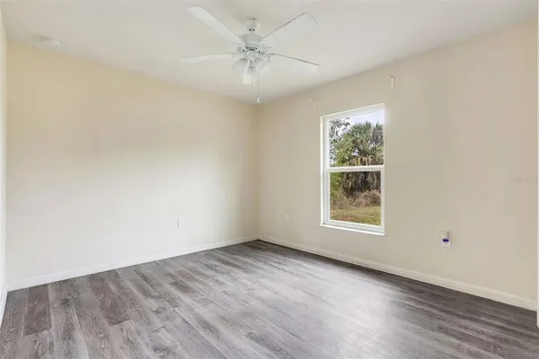 an empty room with wooden floor chandelier fan and windows