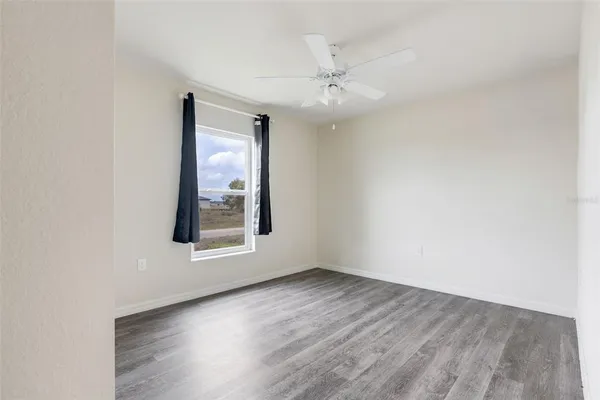 an empty room with wooden floor chandelier fan and windows
