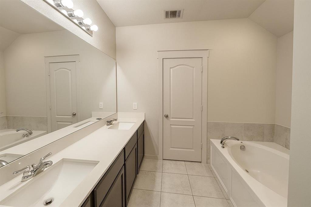 5641 Durst Lane Forney, TX 75126 - Photo 5 of 10 Bathroom featuring a dual vanity with undermount sinks, a large integrated mirror, overhead lighting, and a built-in bathtub with a tiled surround