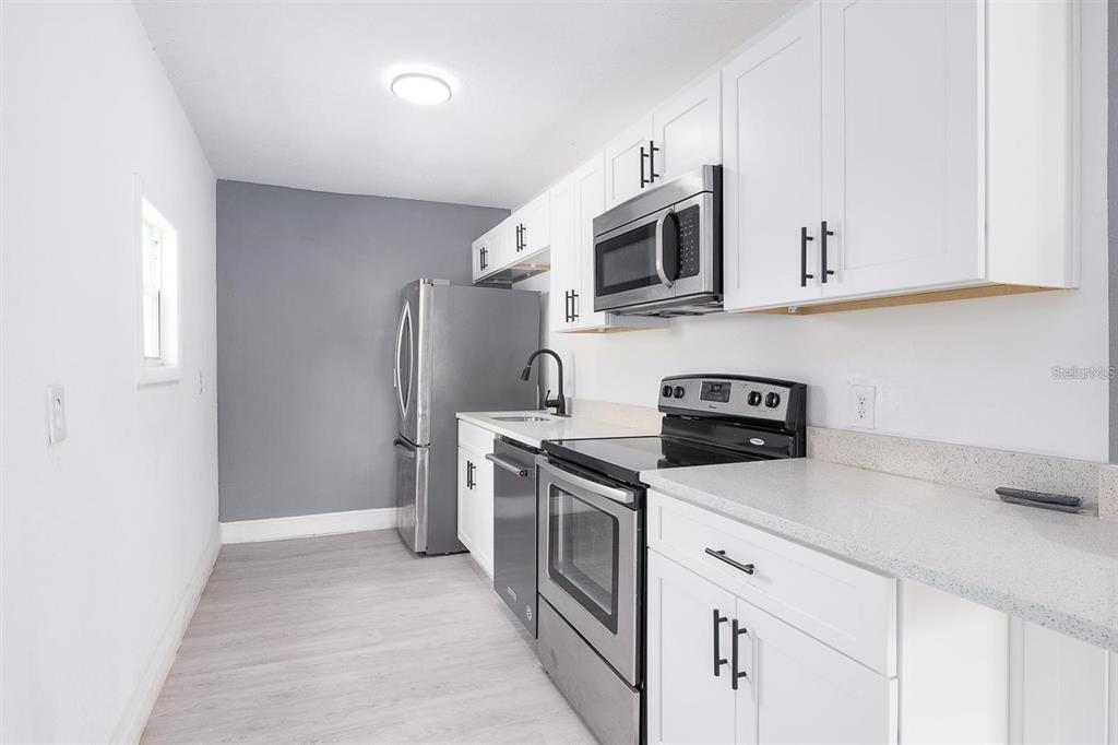 519 Williams Street Melbourne, FL 32901 - Photo 6 of 15 a kitchen with stainless steel appliances granite countertop white cabinets a sink a stove a refrigerator and microwave with wooden floor