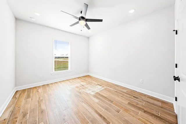 an empty room with wooden floor fan and windows
