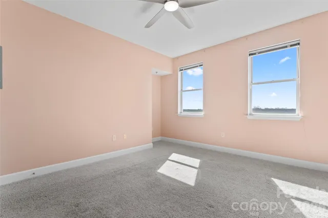 an empty room with a chandelier fan and windows