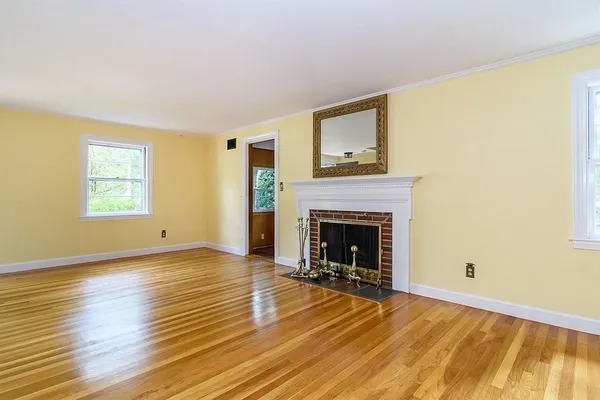 a view of an empty room with wooden floor and a fireplace