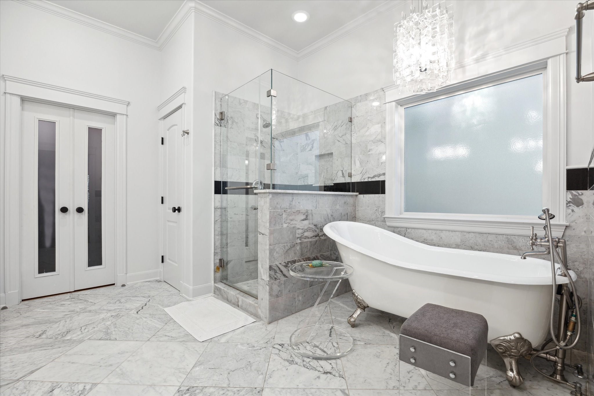 606 Rutland Street Houston, TX 77007 - Photo 35 of 48 Primary bathroom has elegant marble flooring and walls, a spacious glass-enclosed shower, and a luxurious clawfoot tub. It’s bright and modern, with a chic chandelier and frosted window for privacy.