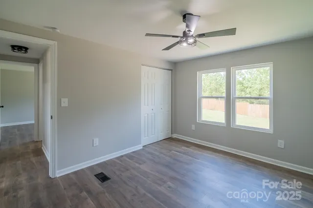 an empty room with wooden floor fan and windows