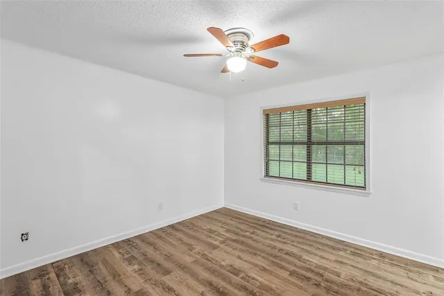 an empty room with wooden floor fan and windows