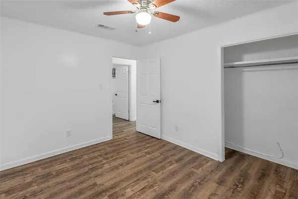 an empty room with wooden floor fan and windows