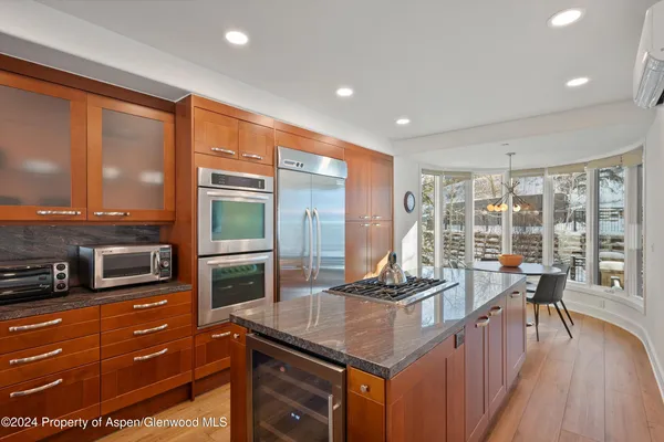 a kitchen with stainless steel appliances granite countertop a stove top oven a sink dishwasher a dining table and chairs with wooden floor