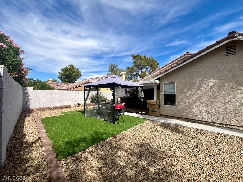 15 Rue Des Champs Henderson, NV 89074 - Photo 23 of 23 An enclosed backyard features gravel landscaping, a patch of lawn, and a tiled roofline.