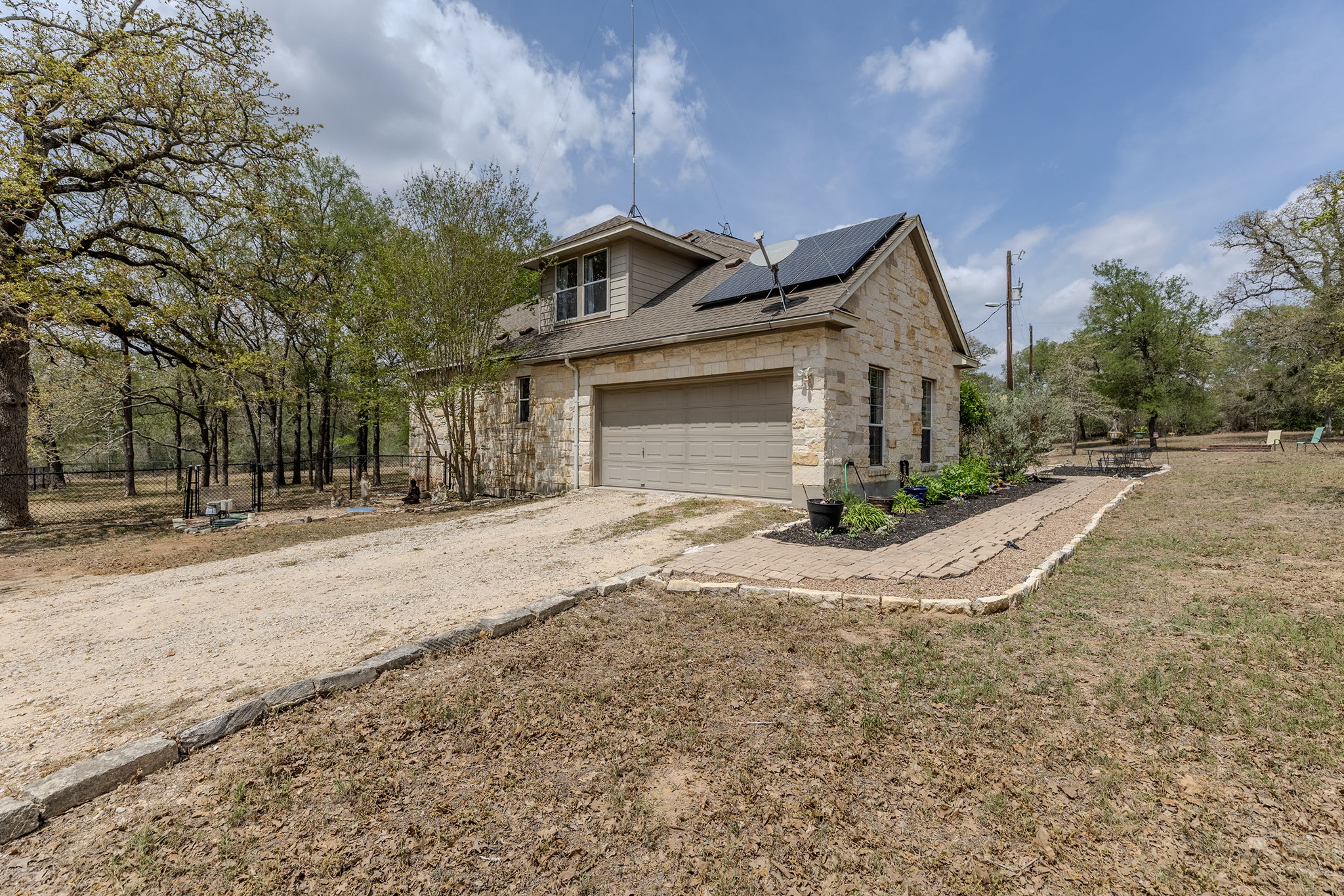 202 The Oaks Boulevard Elgin, TX 78621 - Photo 11 of 40 View of side of home featuring solar panels, stone siding, driveway, roof with shingles, and a garage