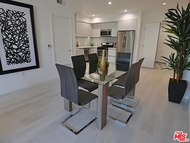 a view of kitchen with stainless steel appliances dining table chairs and white cabinets
