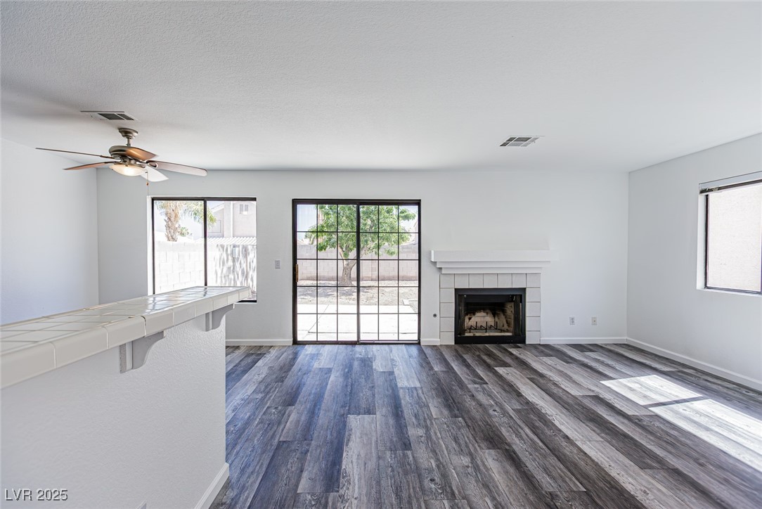 306 Lander Drive Henderson, NV 89074 - Photo 13 of 30 Unfurnished living room featuring dark wood-type flooring, a tiled fireplace, ceiling fan, and a textured ceiling