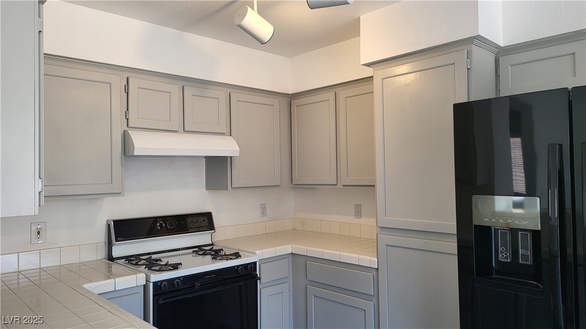 306 Lander Drive Henderson, NV 89074 - Photo 7 of 30 Kitchen with tile countertops, gray cabinetry, white gas range, black refrigerator with ice dispenser, and under cabinet range hood