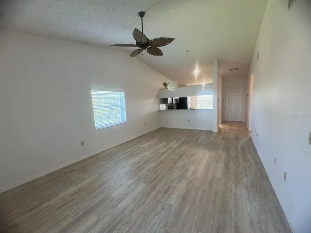 an empty room with wooden floor ceiling fan and windows