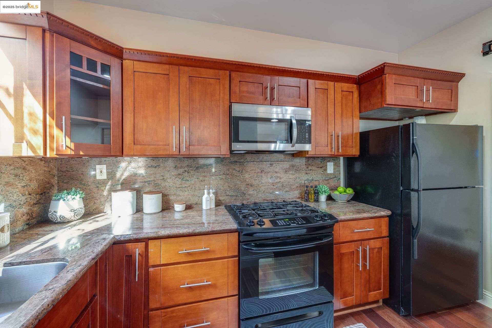 2316 Blake Street, Unit D Berkeley, CA 94704 - Photo 11 of 31 Kitchen with black appliances, tasteful backsplash, brown cabinets, light stone counters, and dark wood finished floors