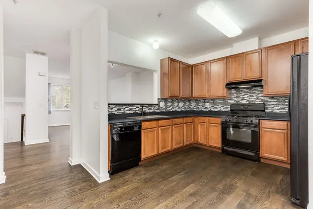 a kitchen with stainless steel appliances granite countertop a stove top oven a sink dishwasher a refrigerator and a microwave oven with wooden floor