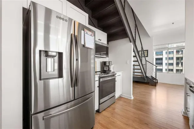 a kitchen with stainless steel appliances kitchen island granite countertop lots of white cabinets and wooden floor