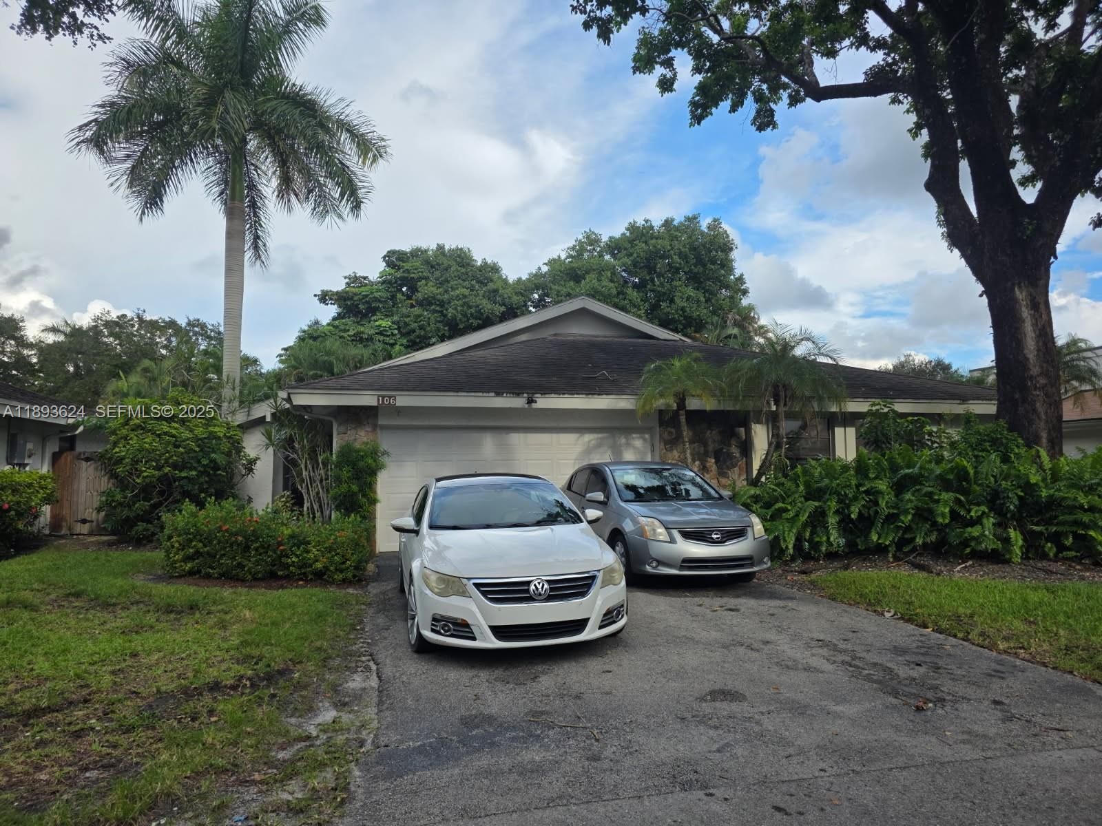 a car parked in front of a house with yard and palm trees