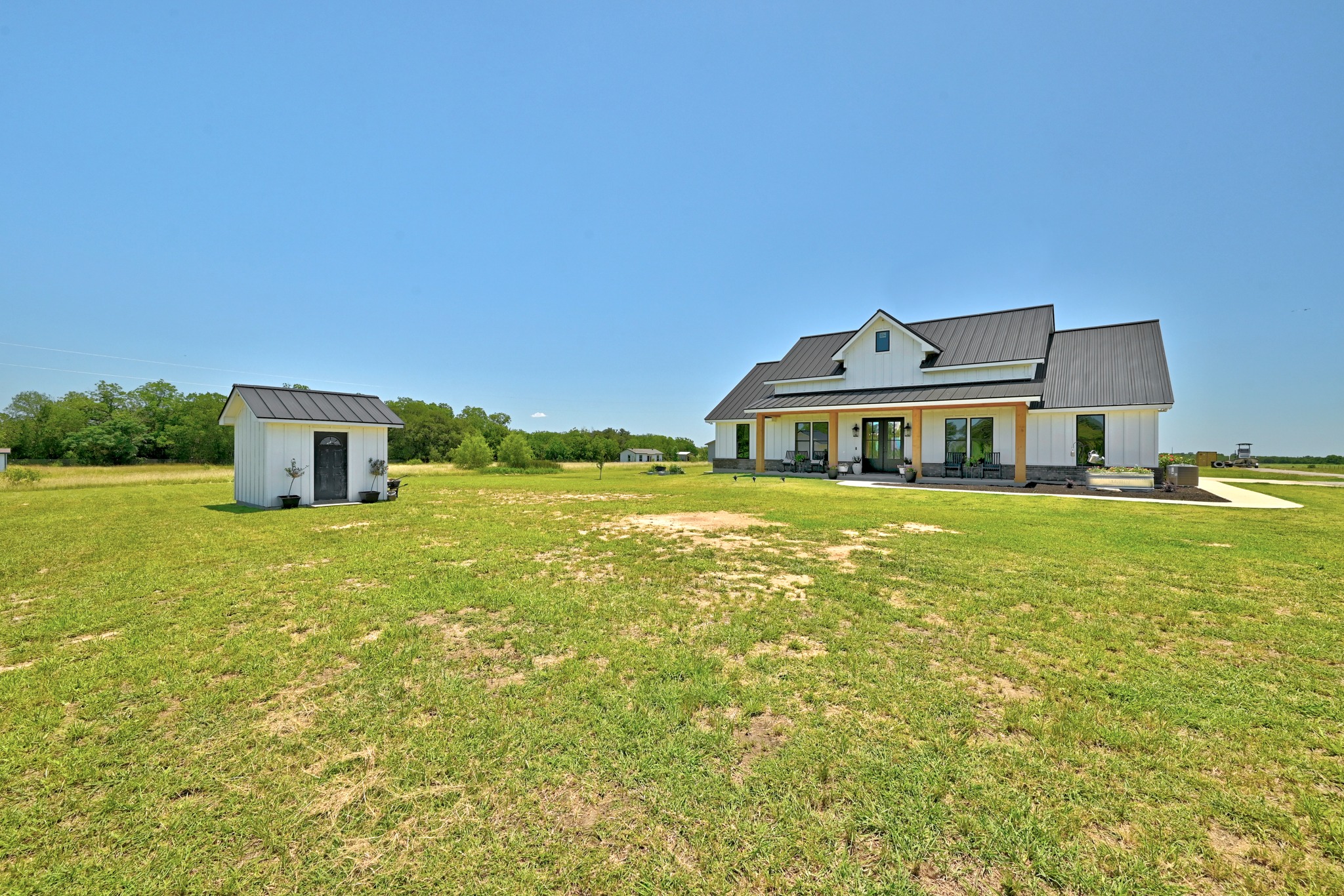2889 Old McMahan Road Lockhart, TX 78644 - Photo 3 of 33 A modern farmhouse with a metal roof and inviting covered porch awaits across a sprawling green yard.