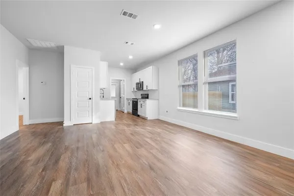 a view of empty room with wooden floor and kitchen view