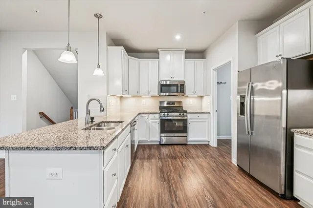 a kitchen with stainless steel appliances granite countertop a refrigerator a sink dishwasher a stove and white countertops with wooden floor