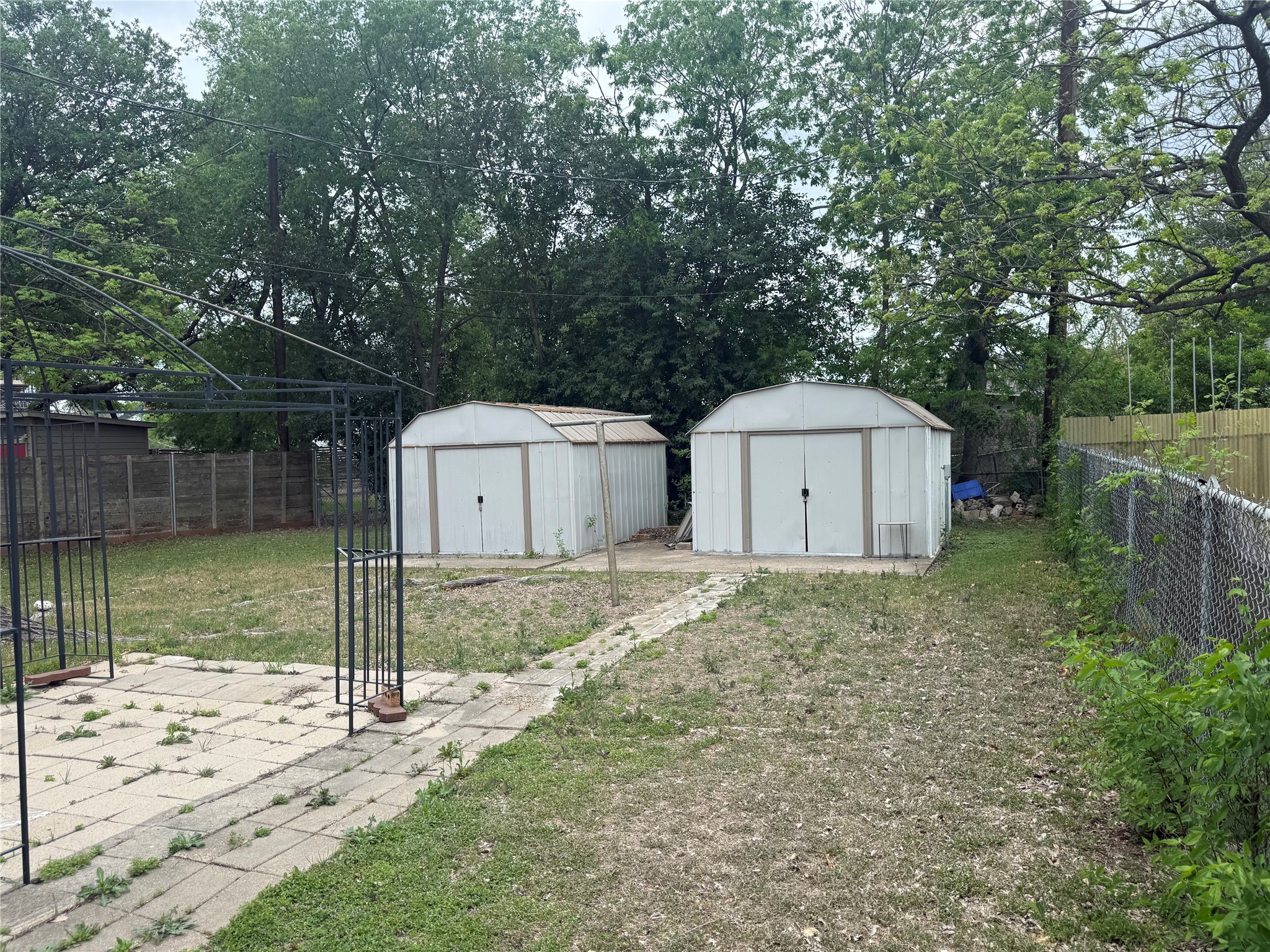 5702 Duval Street Austin, TX 78752 - Photo 11 of 31 Backyard featuring two metal storage sheds, a chain-link fence, and a paved patio area