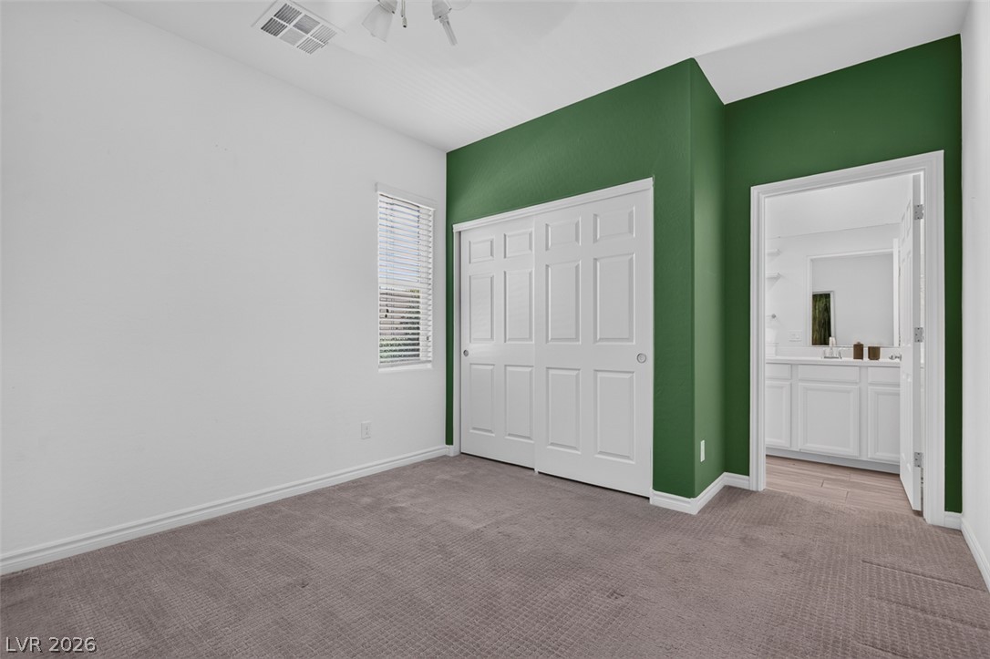 1824 Redland Ridge Street Henderson, NV 89002 - Photo 26 of 69 A well-lit bedroom provides direct access to a private bath, featuring carpet flooring and a neutral color palette with an accent wall.