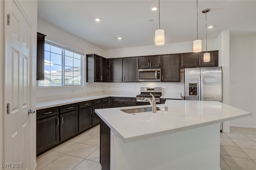 1360 Cerulean Avenue Henderson, NV 89002 - Photo 18 of 62 Kitchen featuring decorative light fixtures, dark brown cabinetry, stainless steel appliances, light stone countertops, and a kitchen island with sink
