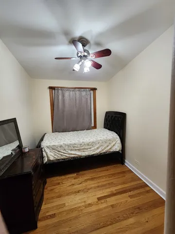 a bedroom with a bed ceiling fan and a wooden floor