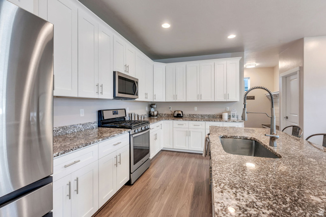 White shaker cabinetry, stainless steel appliances, speckled stone countertops, wood-finish flooring, and recessed lighting