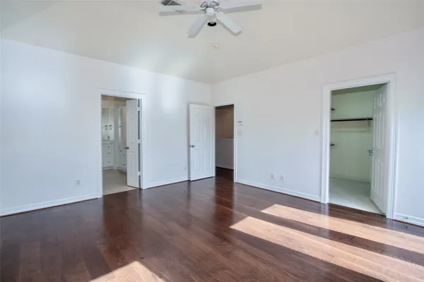 an empty room with wooden floor a ceiling fan and windows