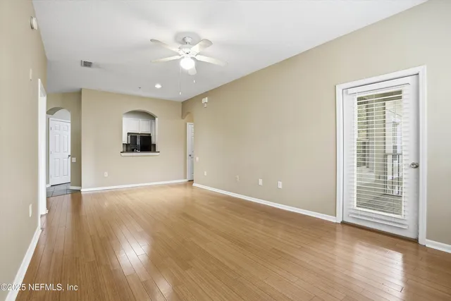 an empty room with wooden floor chandelier fan and windows
