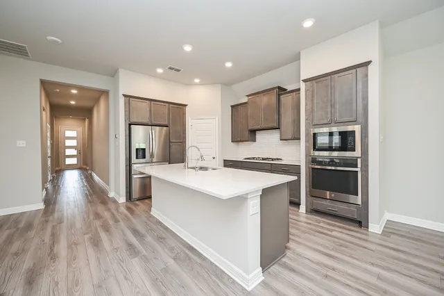 a large kitchen with a center island wooden floor stainless steel appliances and cabinets