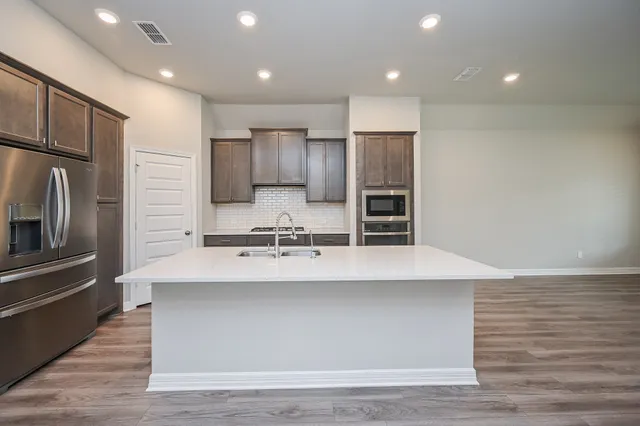 a large kitchen with stainless steel appliances a large counter top a stove and a refrigerator