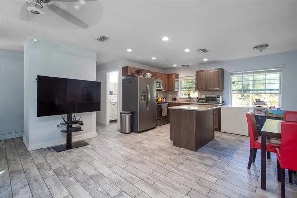 a kitchen with stainless steel appliances kitchen island granite countertop a dining table chairs and a refrigerator