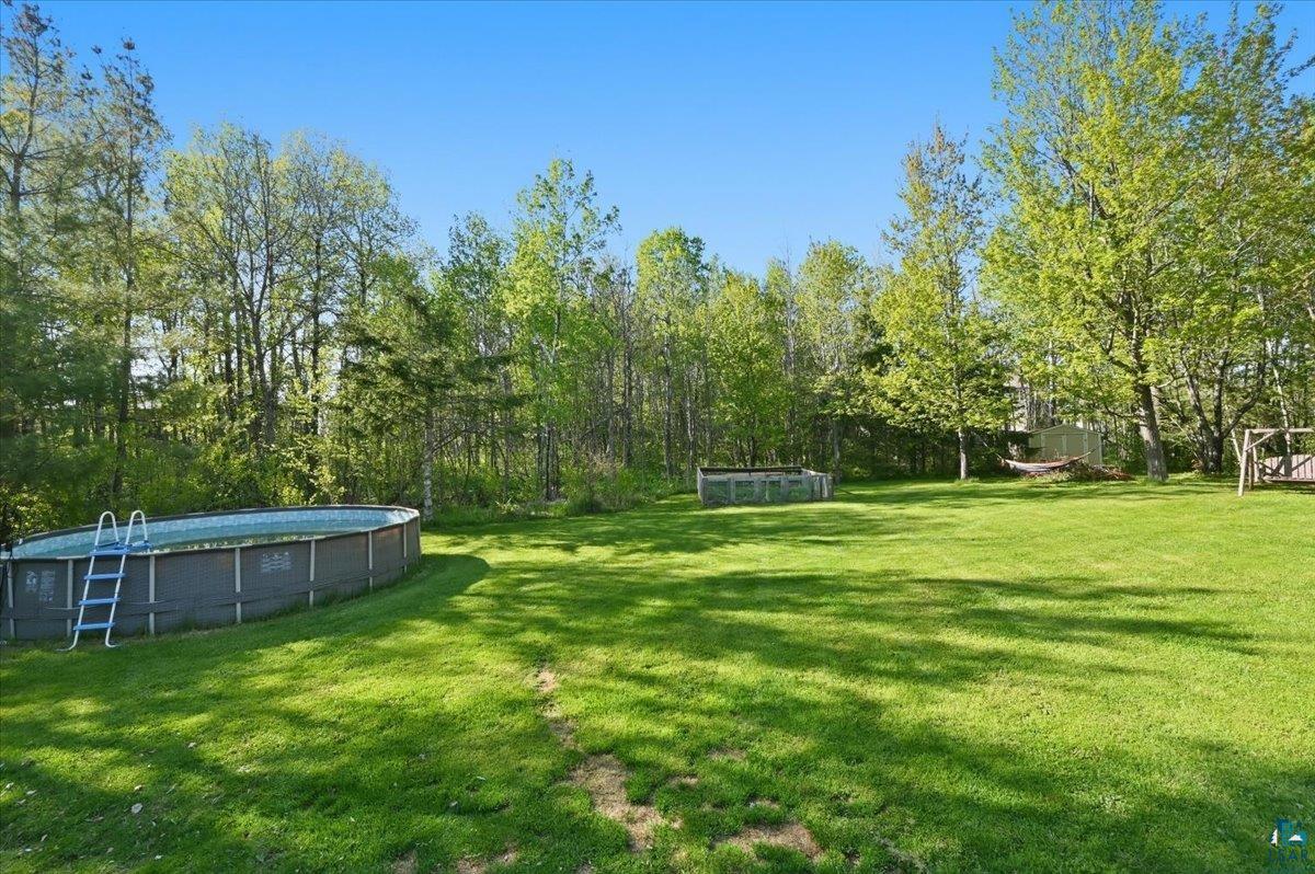 47 Amy Lane Esko, MN 55733 - Photo 26 of 33 Expansive green lawn featuring an above-ground pool with ladder, mature trees, and a wooden swing set