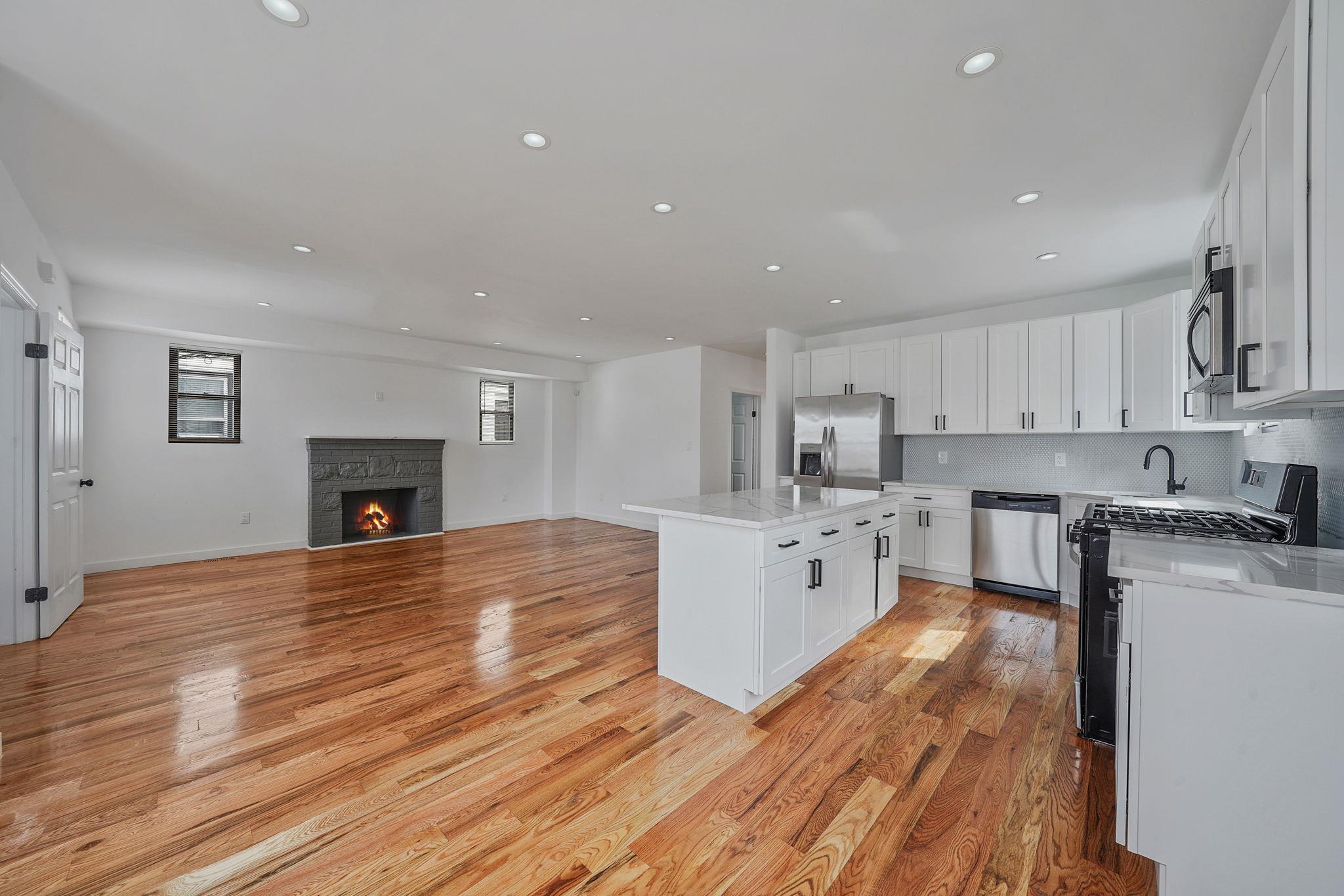 Kitchen with backsplash, a kitchen island, a lit fireplace, light wood-style floors, and stainless steel appliances