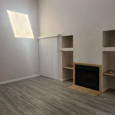 a view of an empty room with wooden floor and a fireplace