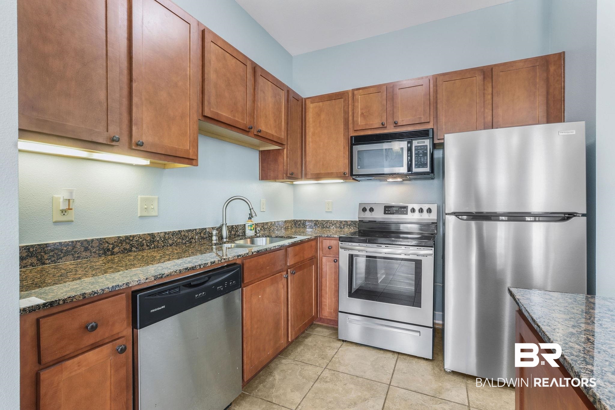 1430 Regency Road, Unit B302 Gulf Shores, AL 36542 - Photo 9 of 24 Kitchen with a sink, dark stone counters, appliances with stainless steel finishes, and brown cabinetry