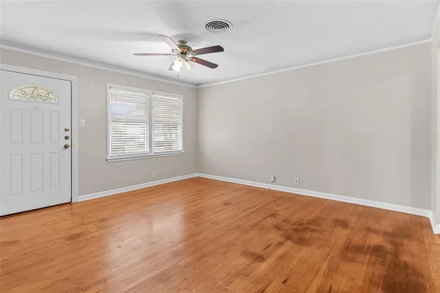 an empty room with wooden floor chandelier fan and windows
