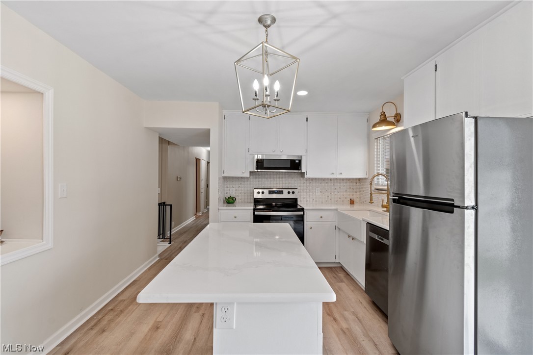 203 Pontius Road Mogadore, OH 44260 - Photo 12 of 26 Kitchen featuring white cabinets, backsplash, a center island, light hardwood flooring, and appliances with stainless steel finishes
