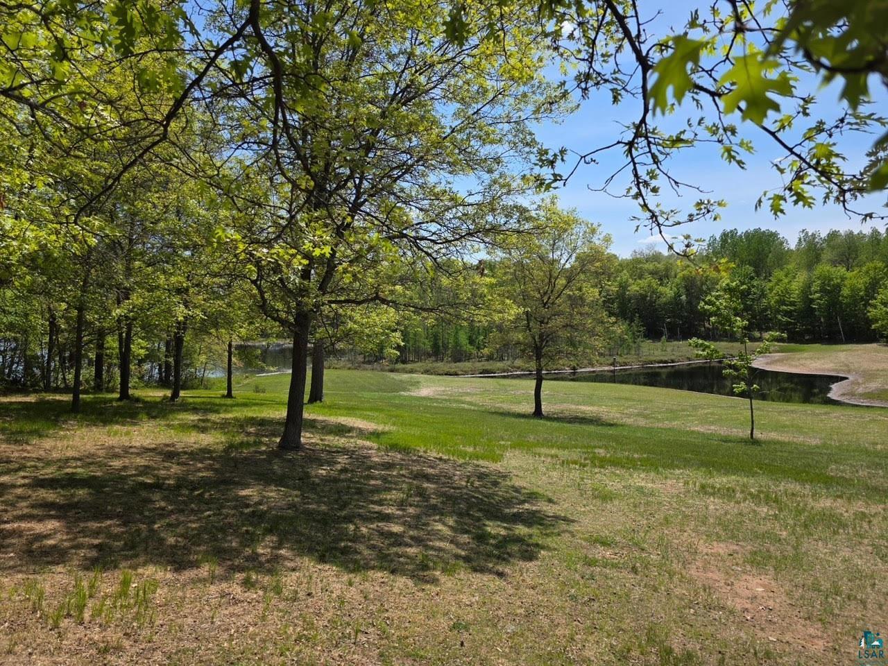 11702 East Mail Road Gordon, WI 54838 - Photo 3 of 49 Expansive green space featuring mature trees and a tranquil pond, bordered by dense woodlands and a clear blue sky