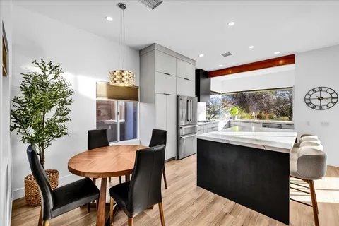 a living room with stainless steel appliances kitchen island granite countertop a table chairs and a large window