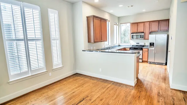 a kitchen with stainless steel appliances granite countertop a stove a sink a refrigerator with wooden cabinets and wooden floor