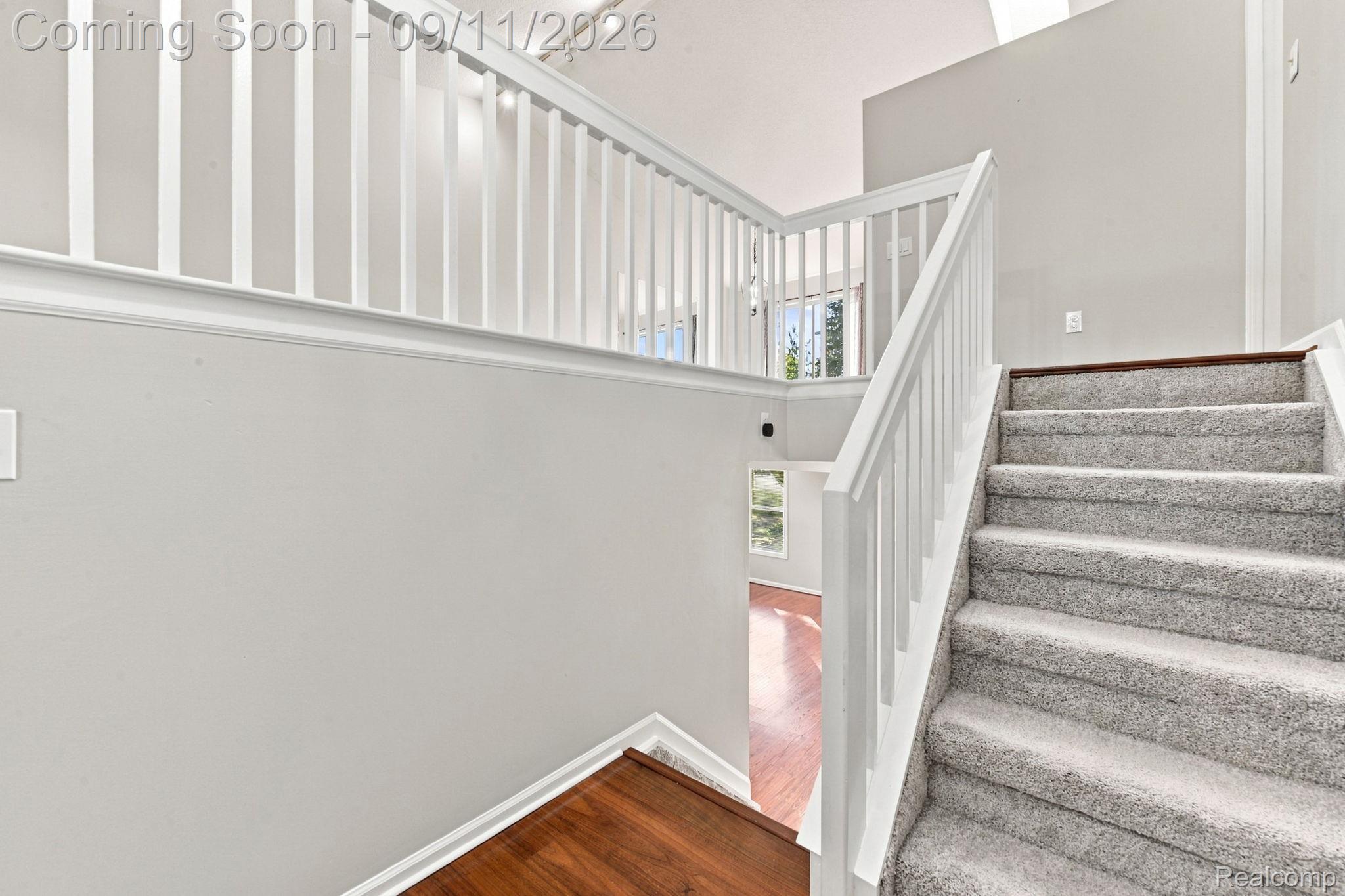 3201 Lynhurst Court Rochester, MI 48306 - Photo 8 of 43 Light gray wall paint, white railings, carpeting on stairs, wood-finish flooring visible below, and vaulted ceiling