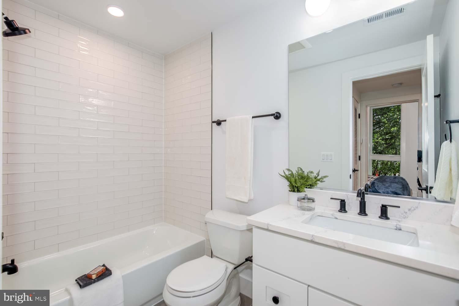 2601 30th Street Northeast, Unit 11 Washington, DC 20018 - Photo 15 of 32 a bathroom with a granite countertop sink a toilet a mirror a bathtub and shower