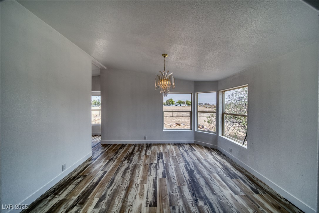 1340 South Adams Road Pahrump, NV 89048 - Photo 21 of 31 Unfurnished dining area featuring a chandelier, a textured ceiling, vaulted ceiling, plenty of natural light, and dark wood-type flooring
